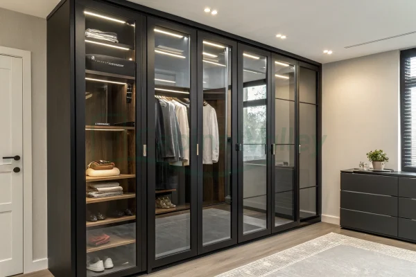 Contemporary black wardrobe with hinged glass doors and integrated LED lighting, showcasing neatly arranged garments, accessories, and open shelving in a minimalist bedroom.