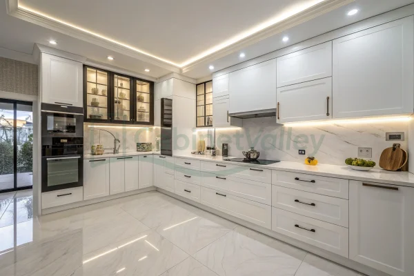 Bright white kitchen with handle-free cabinets, LED lighting, and built-in appliances in a contemporary layout.