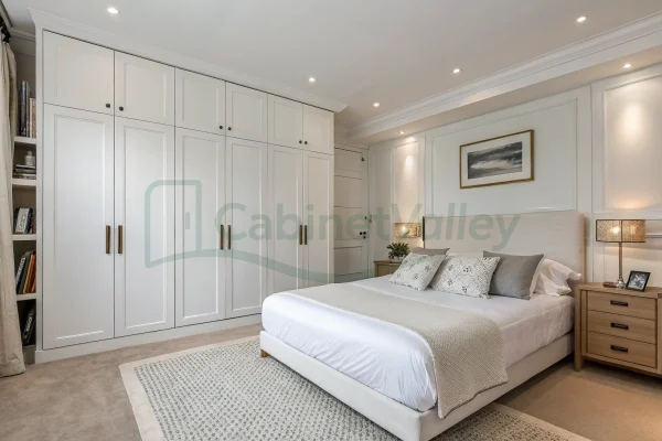 Modern white full-height hinged wardrobe with symmetrical panel doors, integrated into a minimalist bedroom with soft beige tones.