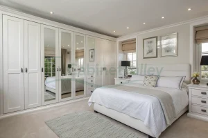 Wall-mounted hinged wardrobe in matte white with mirrored doors and clean molding details, adding brightness and visual depth.