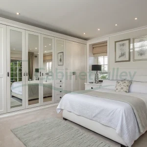 Wall-mounted hinged wardrobe in matte white with mirrored doors and clean molding details, adding brightness and visual depth.