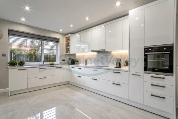 L-shaped kitchen design with white melamine cabinets, glass display units, and modern integrated features.