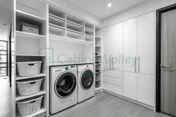 Minimalist laundry room with matte white built-in cabinets, black edge pulls, and open shelving above front-loading machines.